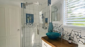 Ein Badezimmer mit Dusche, Waschbecken mit blauer Schale und Spiegel.