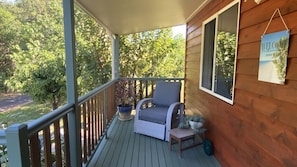 A wooden deck with a wicker chair and a small table, surrounded by greenery. - Mission Dreaming - 1 Bedroom Cottage (South Mission Beach)