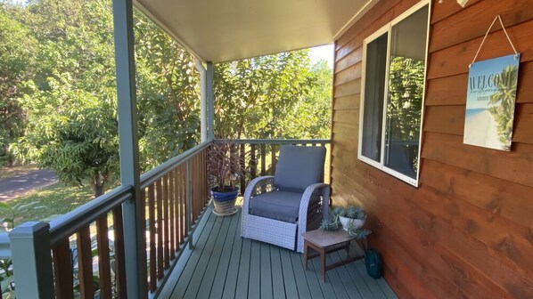 A wooden deck with a wicker chair and a small table, surrounded by greenery. - Mission Dreaming - 1 Bedroom Cottage (South Mission Beach)