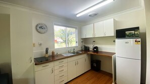 A kitchen with white cabinets, a wooden countertop, a stainless steel sink, a clock, and a refrigerator. - Mission Dreaming - 1 Bedroom Cottage (South Mission Beach)