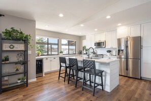 A modern kitchen with white cabinets, a stainless steel refrigerator, and a large island with bar stools.