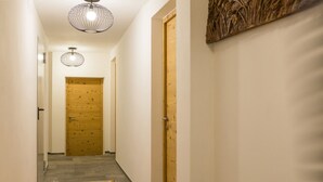 En hall med en trädörr längst in, en mönstrad matta på golvet och en väggmonterad lampa.