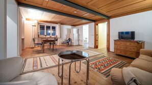 A spacious living room with a wooden ceiling, a dining area with a table and chairs, a television on a dresser, and a patterned rug on the floor. - Apartments Stina 122A (Ortisei)