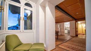 A room with a green armchair, a matching ottoman, and a view of a snowy landscape through a window. - Apartments Stina 122A (Ortisei)