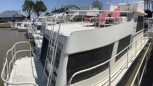Un barco con cubierta protegida, barandillas metálicas y una escalera que lleva a la cubierta superior.