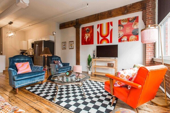 A living room with a checkered rug, a blue sofa, an orange armchair, and a coffee table.