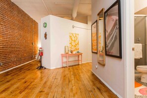 A hallway with a brick wall, wooden flooring, a pink console table, and artwork on the walls.