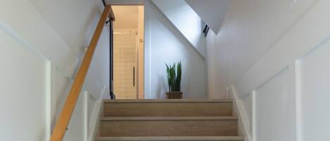 A staircase with wooden steps and white walls, leading to a door at the top.