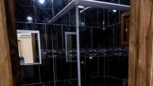 A bathroom with black tiles, a glass shower enclosure, a white sink, and a toilet.
