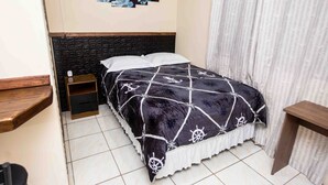 A neatly made bed with a black and white patterned bedspread, a wooden headboard, and a small wooden nightstand.
