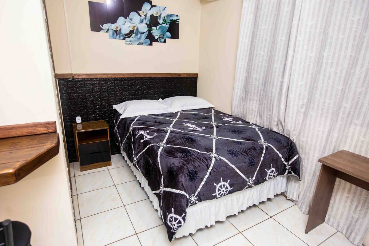 A neatly made bed with a black and white patterned bedspread, a wooden headboard, and a small wooden nightstand.