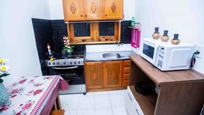 A compact kitchen with wooden cabinets, a stove, a microwave, and a sink.