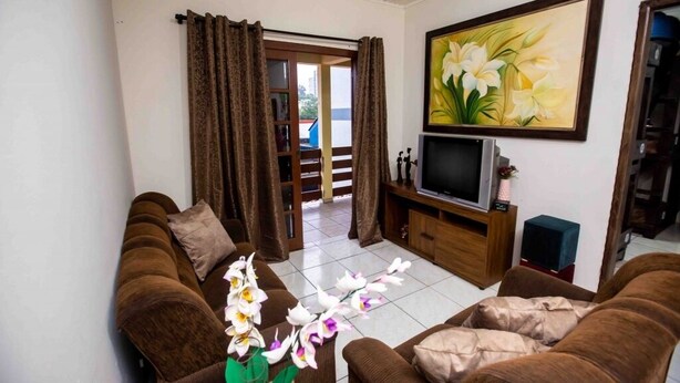 A living room with brown sofas, a TV on a wooden stand, and a painting of flowers on the wall.