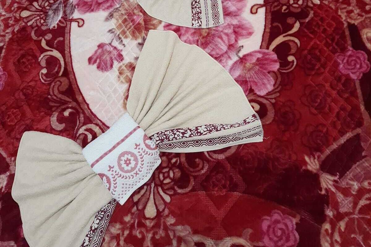 A bed with a red floral bedspread, two beige pillows with decorative bows, and a white pillow with a floral pattern.