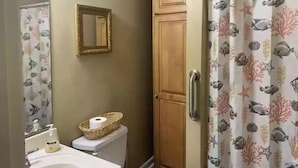 Un baño con inodoro, lavabo, espejo y cortina de ducha con estampado de peces.