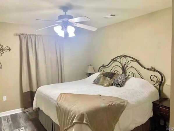 Un dormitorio con una cama, ventilador de techo, mesita de noche y lámpara.