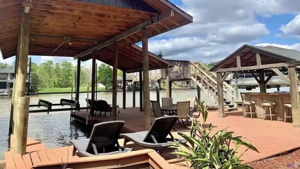 Terraza de madera con sillones de descanso y zona de piscina, rodeada por un pabellón cubierto y una escalera que lleva a una terraza superior.