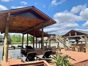 Terraza de madera con sillones de descanso y zona de piscina, rodeada por un pabellón cubierto y una escalera que lleva a una terraza superior.