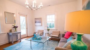 A living room with a glass coffee table, a sofa, a loveseat, a small side table, and a chandelier. - Luxury cottage with pool (Charlottesville)