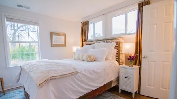 A bedroom with a large bed, a nightstand, a door, and a window. - Luxury cottage with pool (Charlottesville)
