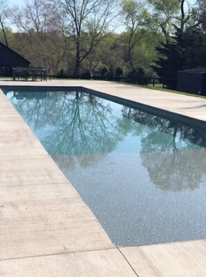 A rectangular swimming pool with a smooth, dark surface, surrounded by a light-colored deck.