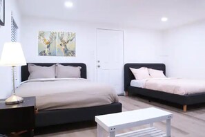 A bedroom with two beds, a bedside table, a lamp, and a painting on the wall. - Cute Small Studio | Trinity Groves (Dallas)