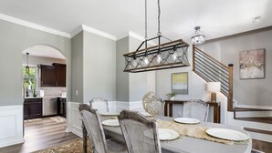 A dining area with a long table, chairs, and a hanging light fixture. - Large luxe home with gorgeous outdoor spaces and hot tub (Fountain Inn)
