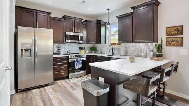 A modern kitchen with dark wood cabinets, stainless steel appliances, and a central island with bar stools. - Large luxe home with gorgeous outdoor spaces and hot tub (Fountain Inn)