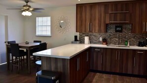 A modern kitchen with wooden cabinets, a large island, and a dining area with chairs. - Cancun Street (Weslaco)