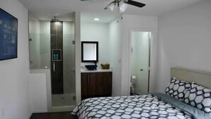 A bedroom with a bed, a ceiling fan, a bathroom with a shower, and a mirror. - Cancun Street (Weslaco)