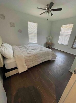 Relax in this serene bedroom with a large bed, ceiling fan, and natural light pouring in through the windows.