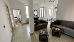 A spacious living area with a herringbone-patterned floor, a sofa, a coffee table, and a dining area with a glass table and chairs. - Crispi 2enty stylish flat at Spanish Steps (Roma)