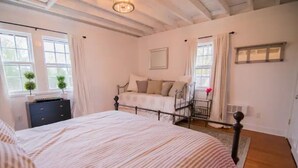 Un dormitorio con una cama grande, un aparador, una ventana con cortinas y una mesita con una planta en maceta.