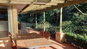 An outdoor covered patio with a wooden table and chairs, surrounded by greenery. - Southern Highland NSW retreat (Fitzroy Falls)