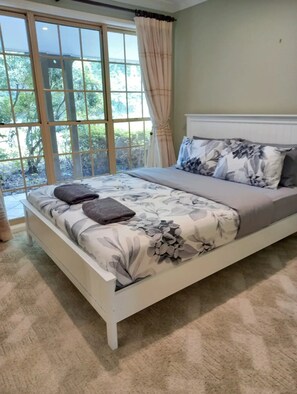 Un dormitorio con cama, ventana con cortinas y vistas al exterior a zonas verdes.