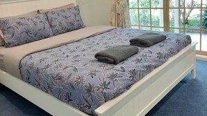 A bedroom with a large bed, a window with curtains, and a view of greenery outside. - Southern Highland NSW retreat (Fitzroy Falls)