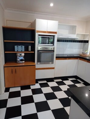 Una cocina compacta con piso a cuadros blanco y negro, gabinetes de madera y horno empotrado.