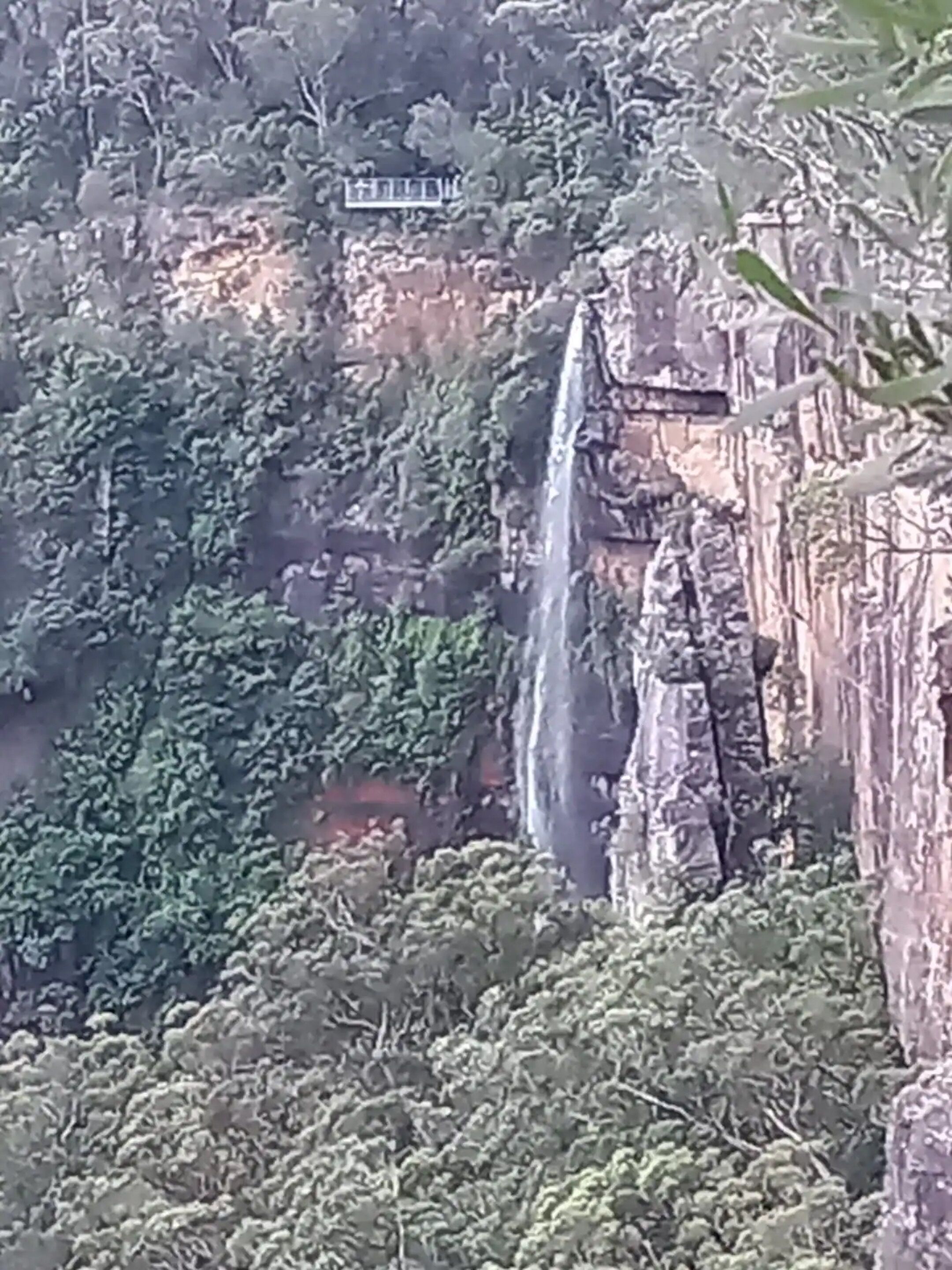 A waterfall cascading down a rocky cliff with a small building at the top.