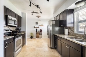 Une cuisine moderne avec des meubles de couleur sombre, des appareils en acier inoxydable, un plan de travail en granit et un revêtement mural en carreaux.