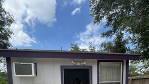 A small, single-story building with a black door and a window with blinds. - Casita Chica (McAllen)