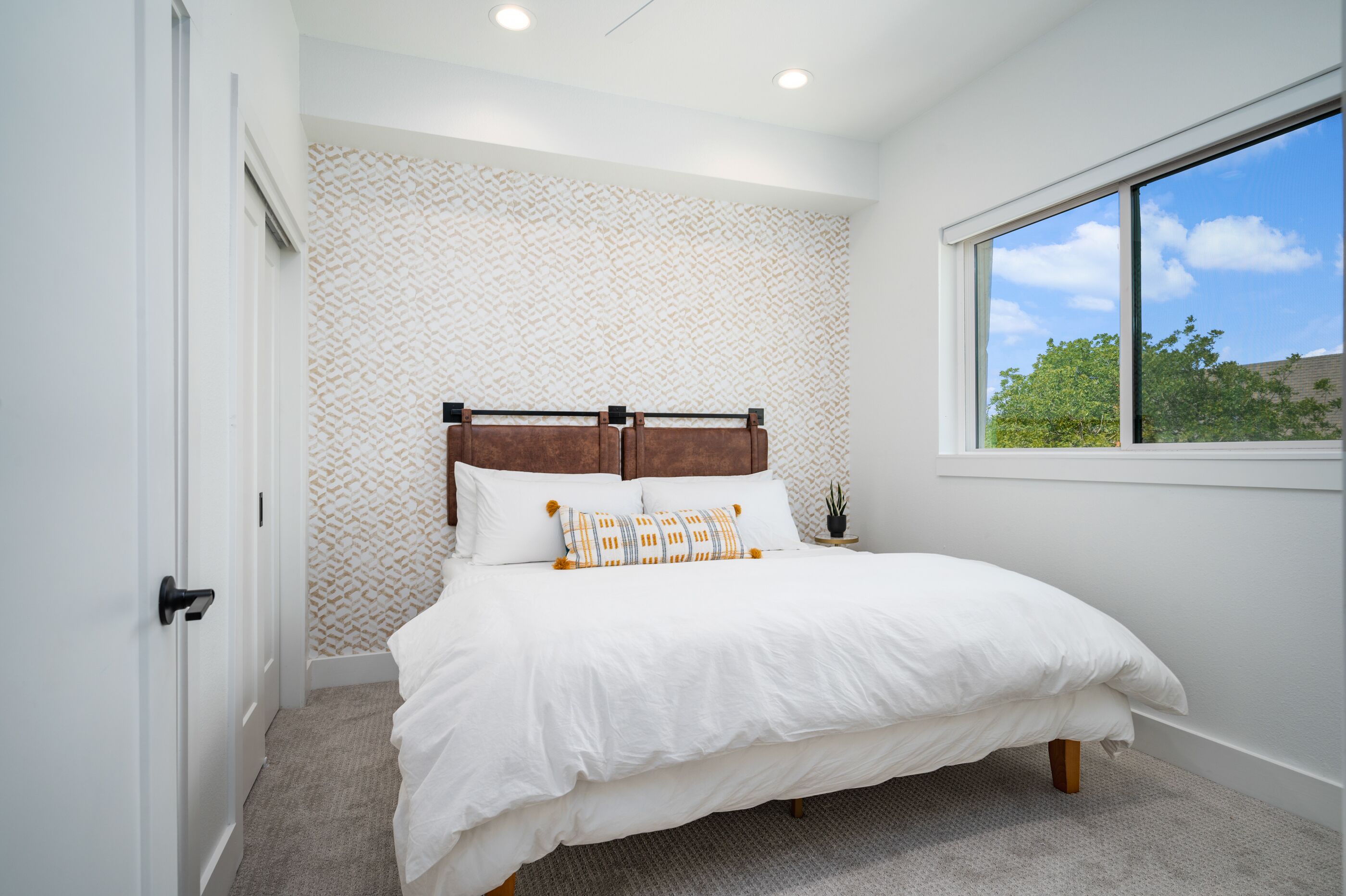 Un dormitorio con una cama grande, un papel tapiz con diseño, una ventana con vistas y una puerta.