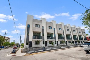 Un immeuble résidentiel à plusieurs étages, doté de balcons, d’un espace de stationnement et surplombant un ciel dégagé.