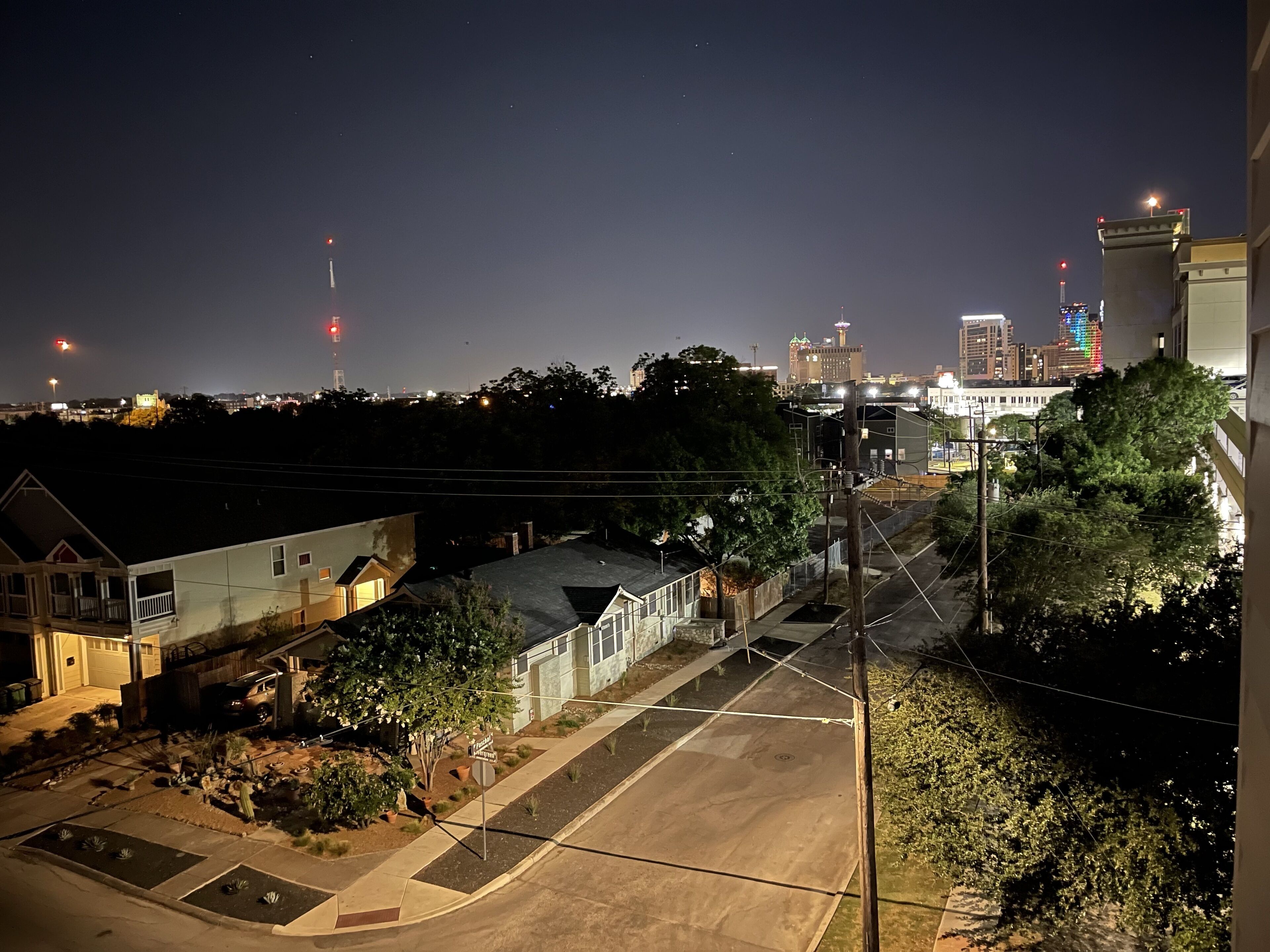 A residential area with houses, a paved road, and a distant city skyline with illuminated buildings.