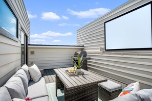 Une terrasse sur le toit avec un canapé, une table sur laquelle se trouve un plateau de boissons et une plante, ainsi qu’un barbecue.
