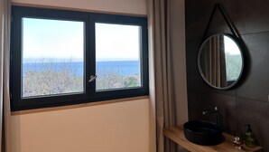 A bathroom with a large window, a round mirror, and a wooden shelf with toiletries. - Casa Prima (Monticello)