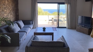 A living room with a sofa, a coffee table, and a TV. There is a stone wall and a view of the outdoors. - Casa Prima (Monticello)