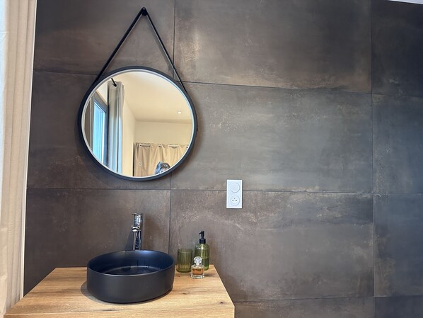 A bathroom with a round mirror, a black sink, and a wooden countertop. - Casa Prima (Monticello)
