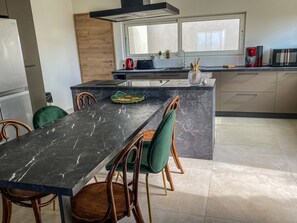 A modern kitchen with a marble countertop, wooden chairs, and a window above the sink.