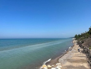 A coastal beach with clear water, rocky shoreline, and sparse vegetation.