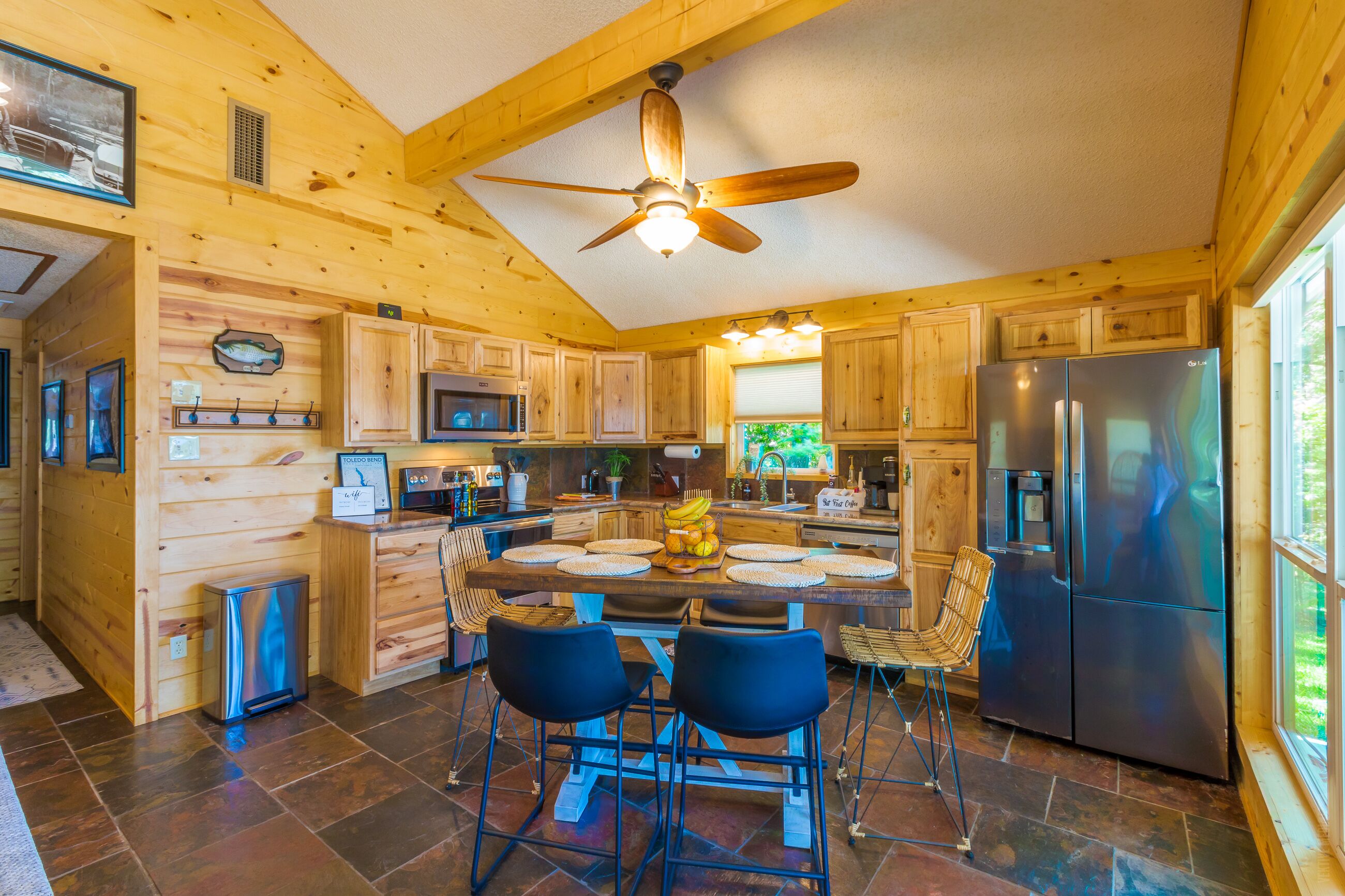 A wooden cabin interior with a kitchen, dining area, and a ceiling fan.